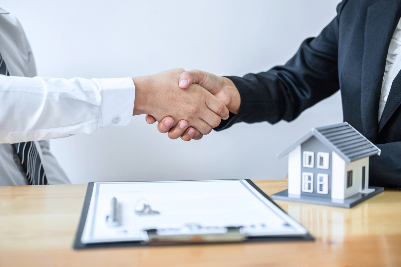Real estate agent are shaking hands after good deal and giving house, keys to customer after discussing and signing contract to buy house with approved application form